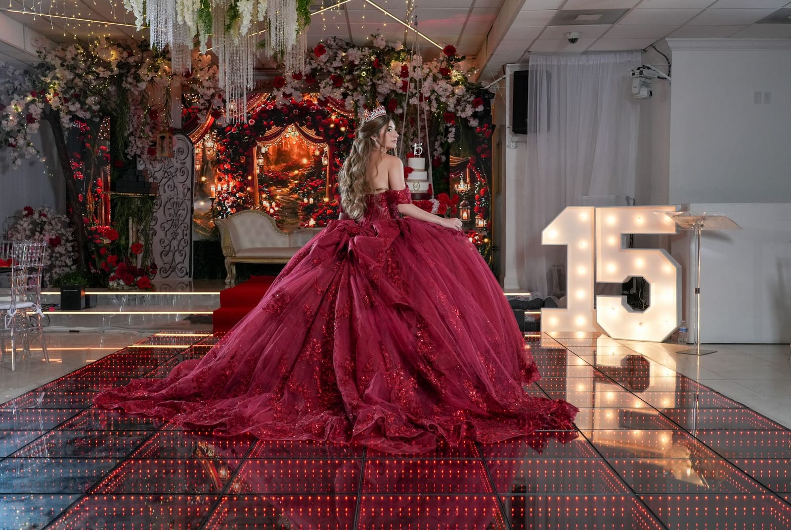 Quinceañera con vestido rojo junto al 15 iluminado